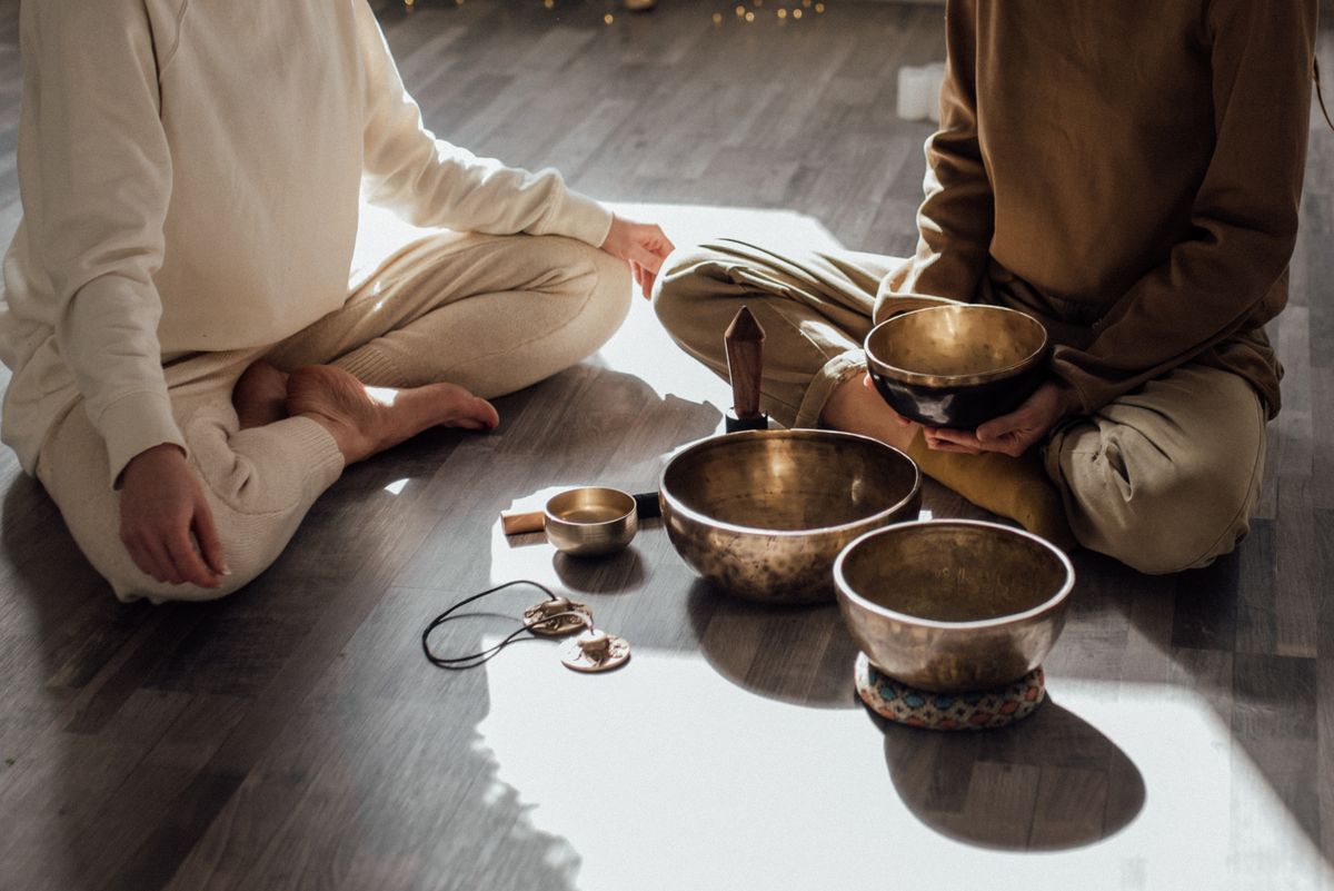 Two people sitting together in sunlight for a shared session, with singing bowls between them